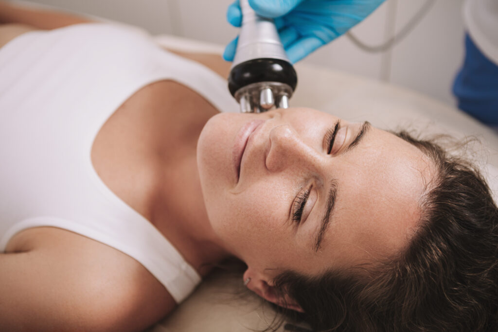 Close up of a cheerful mature woman enjoying facial rf-lifting procedure at beauty salon. Attractive female relaxing during rf-lifting treatment by cosmetologist